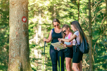 Group of hikers looks at a map beside a tree with a hiking trail sign