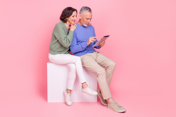 Full body photo of two idyllic partners sit podium use wireless tablet isolated on pink color...