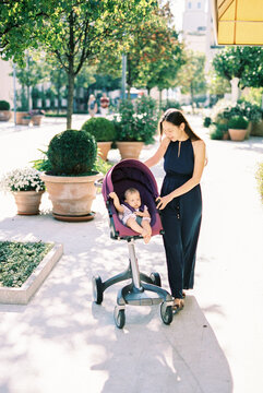 Mom stands near the stroller with the baby on the street near the flowerpots