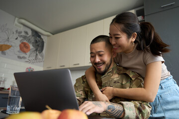 Asian woman in kitchen room hugging from back of military