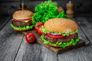 Two delicious homemade burgers of beef on an old wooden table. Fat unhealthy food close-up.