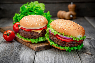 Two delicious homemade burgers of beef on an old wooden table. Fat unhealthy food close-up.