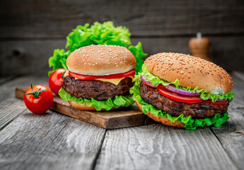 Two delicious homemade burgers of beef on an old wooden table. Fat unhealthy food close-up.
