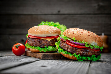 Two delicious homemade burgers of beef on an old wooden table. Fat unhealthy food close-up.