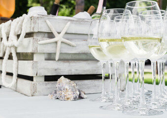Organization of a buffet in the summer. On a table covered with a white tablecloth there are glasses with white wine against the background of a wooden box with ice and bottles of wine.