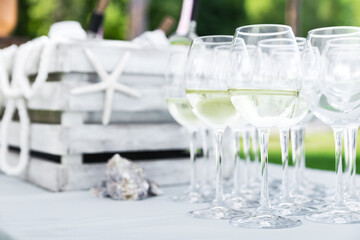 Organization of a buffet in the summer. On a table covered with a white tablecloth there are glasses with white wine against the background of a wooden box with ice and bottles of wine.