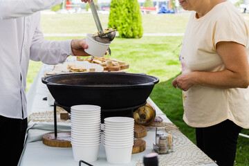 The waiter pours the guest's fish soup into a disposable paper plate. Catering job