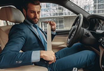 Handsome male fastening seat belt before driving car