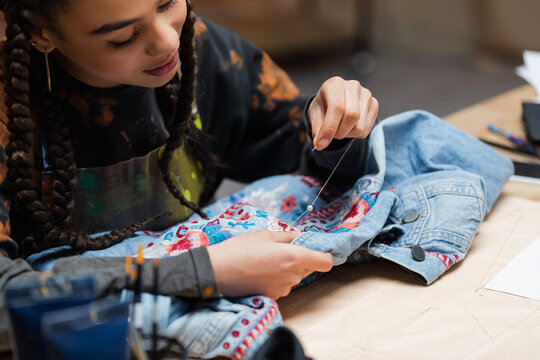 African american designer decorating denim jacket with embroidery in workshop.