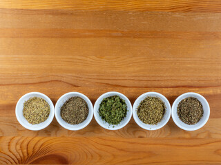 Obraz na płótnie Canvas dried herbs for Mediterranean cooking in white bowls on a wooden table background