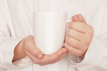 Woman hands holding mock up white cup, mug close-up on beige background. Blank template, logo, text design, promotional, text message.