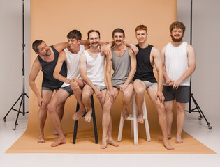 Six young men of different ages having photo shoot at studio. Feeling happy, cheerful and...