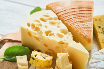 Piece of maasdam cheese and camembert, smoked cheese, blue cheese, parmesan, brie cheese with basil and pepper on white marble board white wooden old background. Set or assortment cheeses. Top view.