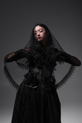 young asian model in gothic outfit with black veil posing isolated on grey.