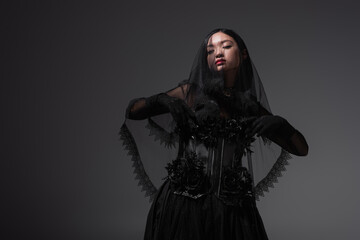young asian woman in gothic outfit with black veil posing isolated on grey.
