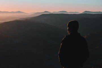 Man from behind standing and looking away at the mountains landscape in morning