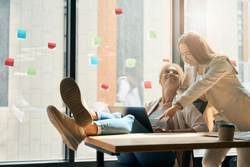 Smiling women watching laptop while sitting at table in coworking