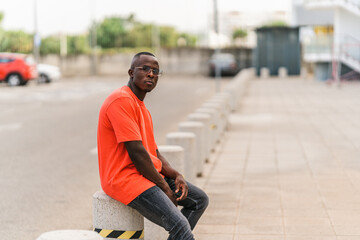 Chico negro joven rapado con camiseta roja posando en la calle estilo urbano