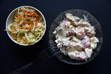 Delicious salad of mayonnaise and vegetables in a plate. Salads of meat and vegetables on a black background.