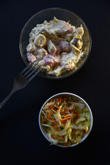 Delicious salad of mayonnaise and vegetables in a plate. Salads of meat and vegetables on a black background.