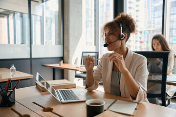 Young woman in headphones with headset communicates with client online in office