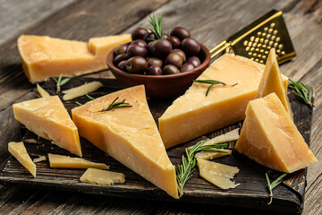 Parmesan cheese on a wooden board, Hard cheese, olives, rosemary and metal grater. place for text, top view