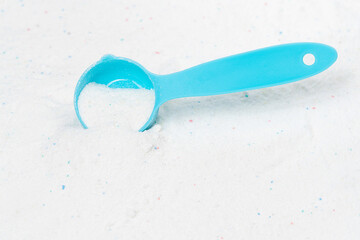 Laundry detergent for washing machines and a plastic scoop for dosing. Washing powder with measuring spoon. White wash powder with with colored granules