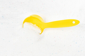 Laundry detergent for washing machines and a plastic scoop for dosing. Washing powder with measuring spoon. White wash powder with with colored granules