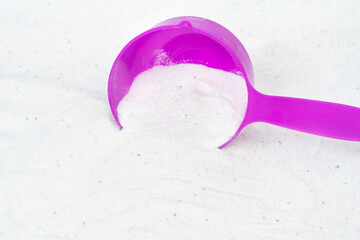 Laundry detergent for washing machines and a plastic scoop for dosing. Washing powder with measuring spoon. White wash powder with with colored granules