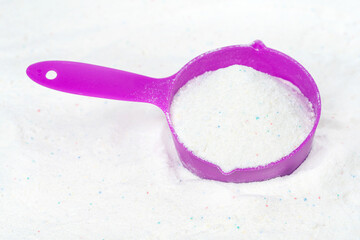 Laundry detergent for washing machines and a plastic scoop for dosing. Washing powder with measuring spoon. White wash powder with with colored granules