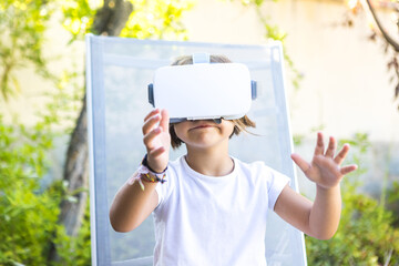 Little girl with virtual reality glasses, trying to touch something in a virtual way, sitting on a...