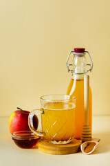 Apple Cider Vinegar in Glass Mug and Bottle with Honey and Cinnamon Red Apples Yellow Background Vertical