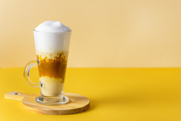 Pumpkin Spice Latte in a Glass Mug with Cinnamon on Wooden Cutting Board Tasty Autumn Drink Yellow Background Horizontal Copy Space