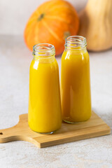 Two Bottles of Pumpkin Juice on Wooden Cutting Board Raw Whole Pumpkin Autumn Healthy Diet Drink Vertical