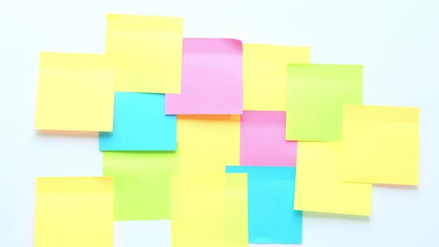 A hand sticks a colorful pieces of paper for notes on a white surface