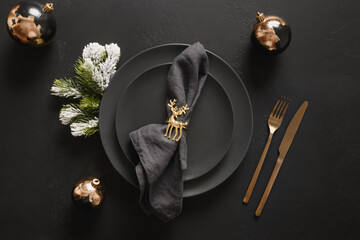 New year table setting with black plate , golden decorations, deer towel ring and cutlery on black background. View from above. Festive holiday.
