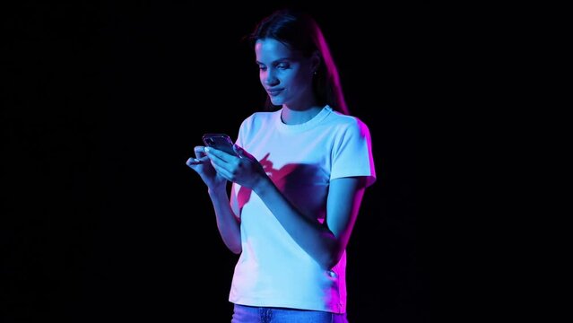 Young excited girl scrolling phone screen and shouting with delight isolated over dark background in neon light. Concept of business, black friday sales