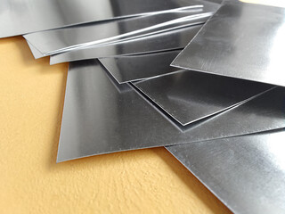 square aluminum on yellow cardboard. pile of thin metal industrial materials. set of square pieces