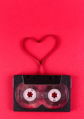 Vertical photo of audio cassette with a film heart on a pink background. Valentine's Day. Symbol of love