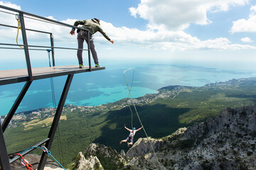 Extreme athlete tied to a safety rope jumped into the void from a mountain, rear view. Ropejumping.