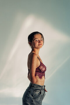 Smiling young woman with amputee arm and scars from burn on her body poses in lacy bra.