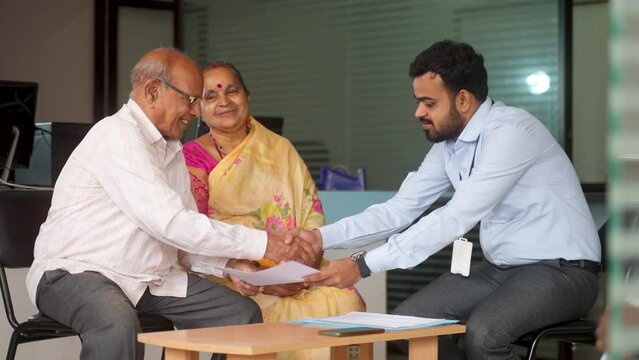 Banker receiving insurance or mortgage documents from senior couple by greeting at bank - concept of financial advisor, support and banking service