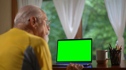 Over shoulder view of senior elderly man making video call on laptop green screen talking and...