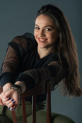 attractive brunette model sitting on a old chair posing and looking at camera on grey background