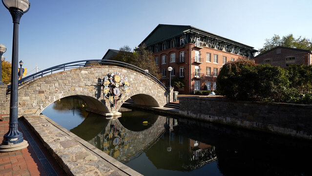 Day time autumn view of bridge in popular city park, Carroll Creek Park in historic district of Frederick Maryland with shops and building on sides of the canal. People walking.