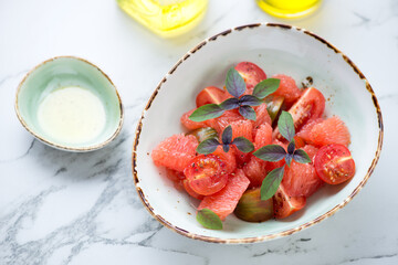 Salad with grapefruit, tomatoes and basil served in a green bowl on a light-grey marble background, horizontal shot