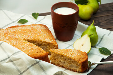 sweet pear pie and a cup of milk on the table. home baking concept. pear cake on a wooden background. biscuit fruit cake on a brown surface