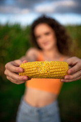 Girl with corn in a cornfield. The girl eats corn on the background of the corn field. A beautiful girl with curly hair and freckles eats.