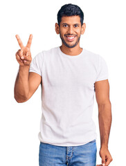 Fototapeta premium Young latin man wearing casual clothes smiling looking to the camera showing fingers doing victory sign. number two.
