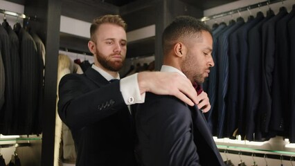 Over shoulder view of bearded fashion designer fitting bespoke suit to model, close-up shot